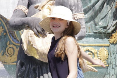 Portrait of smiling girl in hat by statue