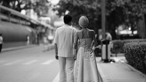 Rear view of couple walking on sidewalk in city