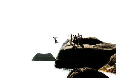 People standing on rock formation against clear sky