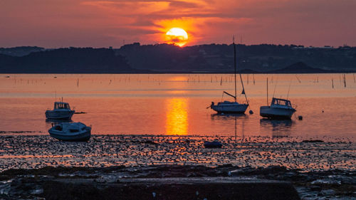 Sailboats moored on sea against orange sky
