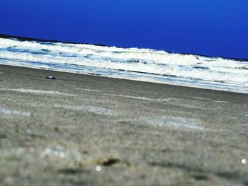 Close-up of waves on beach against clear blue sky