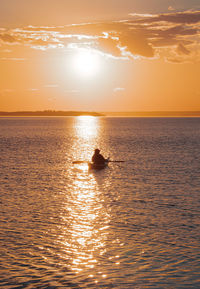 Silhouette person in sea against sky during sunset