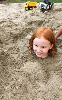 High angle view of redhead girl buried in sand at playground