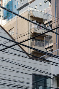 Many electric wires intersect and there are many buildings in the background.