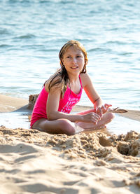 Young girl holds a bird feather, as she decorates a sand castle on the beach