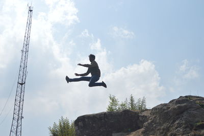 Low angle view of man jumping on rock against sky