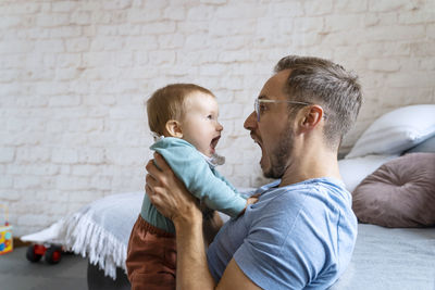 Playful father screaming with baby boy at home