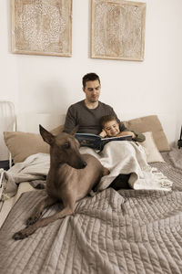 Father and son reading a book on the bed at home. young attractive man and little boy with dog 