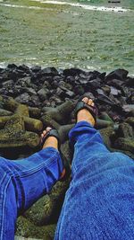 Low section of man sitting on rock by sea