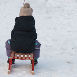 Rear view of child sitting on stool over snowy field