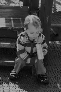 High angle view of boy holding drink can while sitting on steps