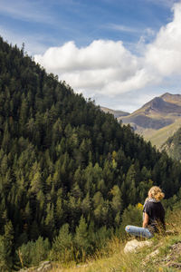 Rear view of woman man sitting on mobile phone against sky