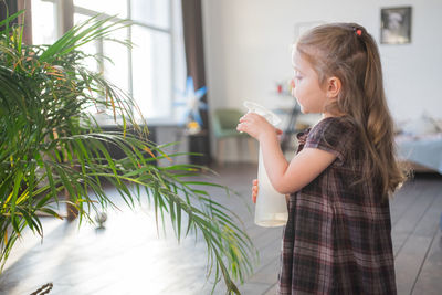 Cute girl watering plant at home