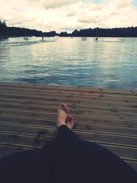 Low section of man sitting on pier over sea against sky