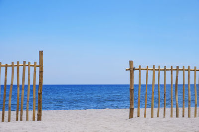 Wooden posts on beach against clear blue sky