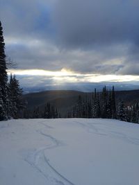 Snow covered landscape against cloudy sky