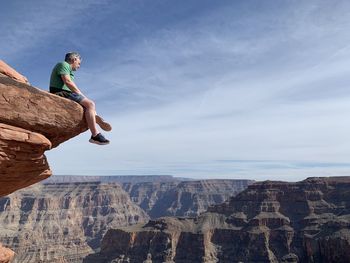 Side view of man on rock against sky