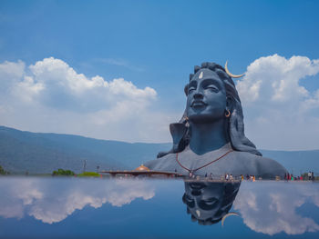 Statue by lake against sky