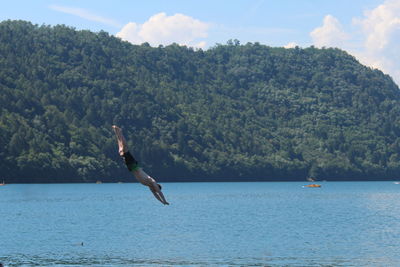 Man jumping in sea against mountain