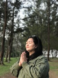 Smiling woman praying while standing in forest