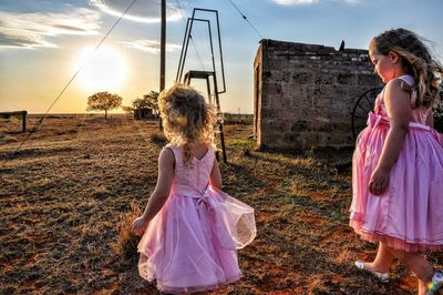 Sisters wearing pink dress while walking on field during sunset