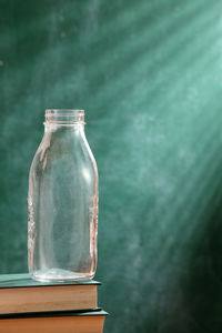 Close-up of glass bottle on books against blackboard in classroom