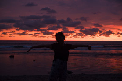 Silhouette woman standing at beach against sky during sunset