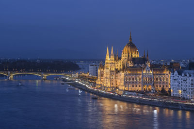 Illuminated bridge over river against sky in city