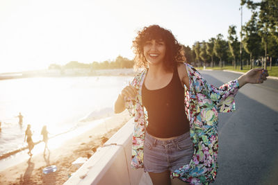 Portrait of beautiful woman standing by retaining wall at beach