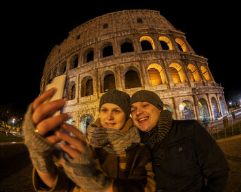 Happy couple taking selfie against coliseum at night