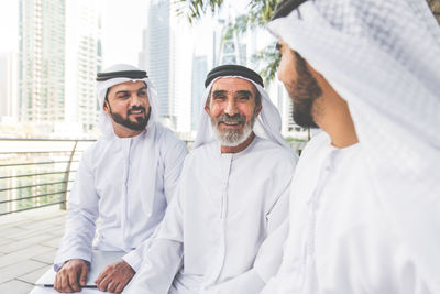 Smiling senior man with grandsons wearing dish dash sitting outdoors