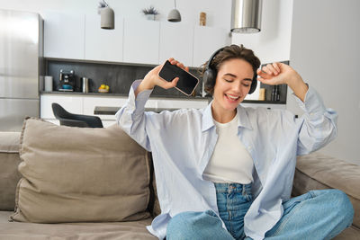 Portrait of young woman using mobile phone while sitting on sofa at home