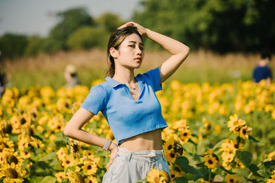 Portrait of young woman standing amidst yellow flowering plants on field