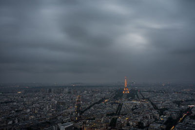 Distant view of eiffel tower amidst cityscape against cloudy sky at dusk
