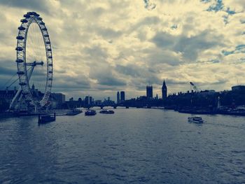 Ferris wheel in city against cloudy sky