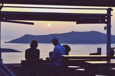 Rear view of silhouette men sitting on table by sea