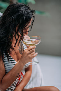 Midsection of woman drinking glass while sitting outdoors