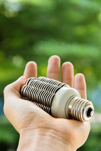 Cropped hand of man holding light bulb against plants