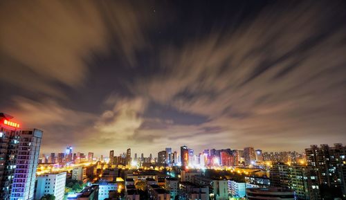 Illuminated cityscape against cloudy sky at night