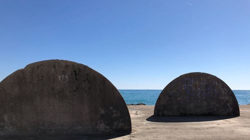 Rocks on sea shore against clear blue sky