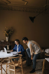 Non-binary person using laptop by boyfriend getting ready at home