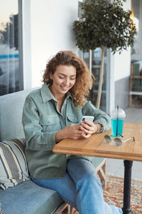 Smiling young woman using phone at cafe