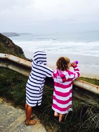 Rear view of siblings standing on beach against sea