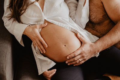 Midsection of couple sitting on sofa at home