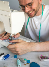 A smiling blond man in glasses is sewing in home workshop. a seamster with a sewing machine