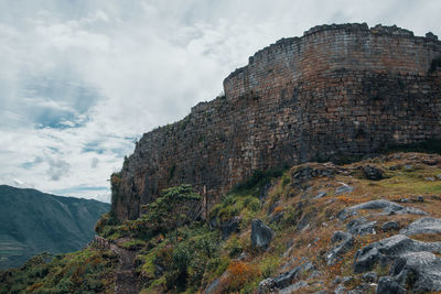 Low angle view of ancient wall against cloudy sky