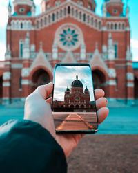 Close-up of hand holding smart phone against building