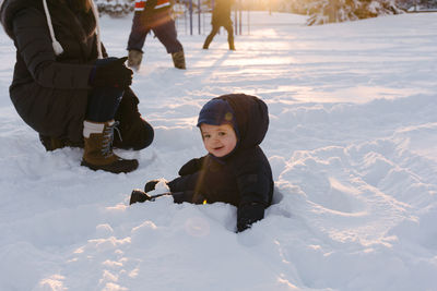 Full length portrait of happy baby boy sitting on snow covered landscape