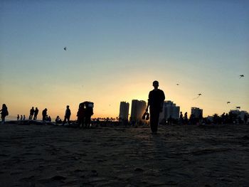 Silhouette people at beach against clear sky during sunset