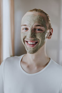 Happy young make-up artist with facial mask at home